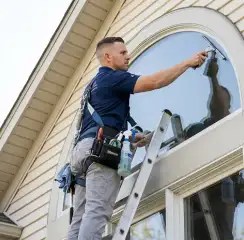 Professional window cleaner on a ladder using a squeegee to clean an exterior arched window, Akron, OH.